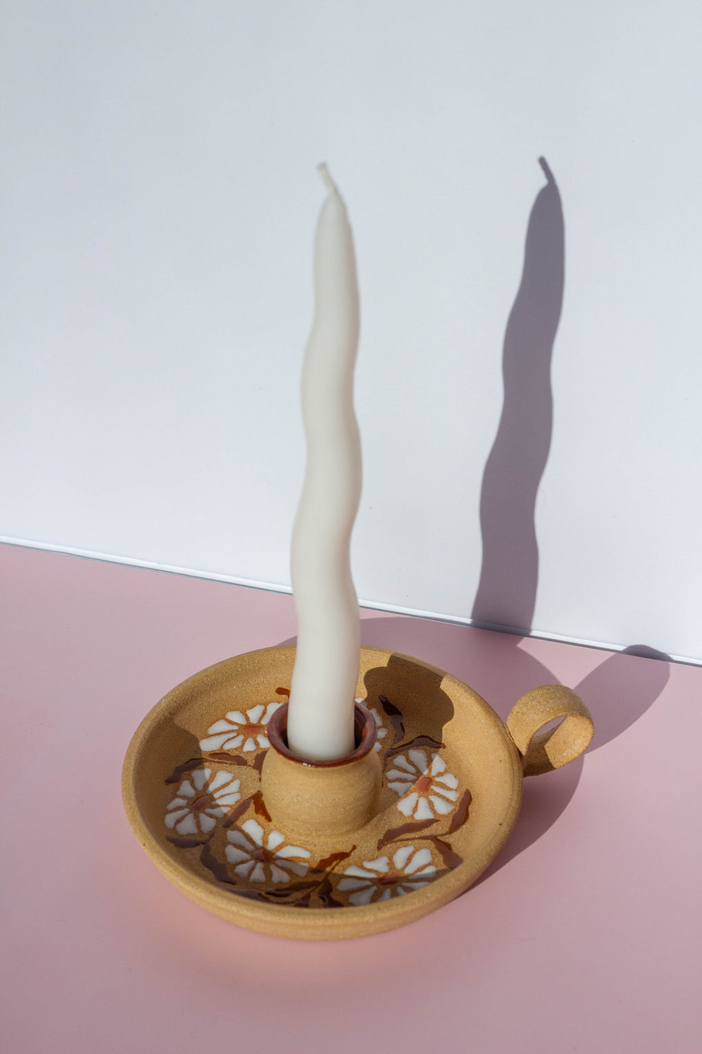 Ceramic candle holder with a single white candle on a pink surface and white background