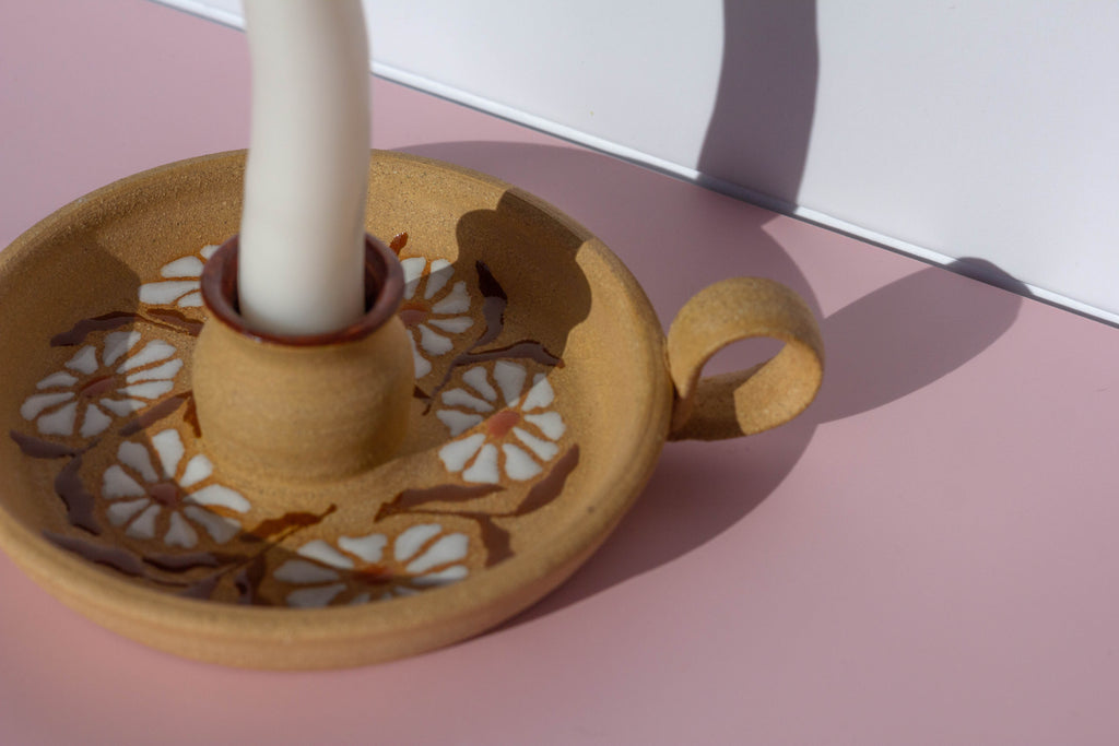 Ceramic candle holder with floral designs on a pink surface
