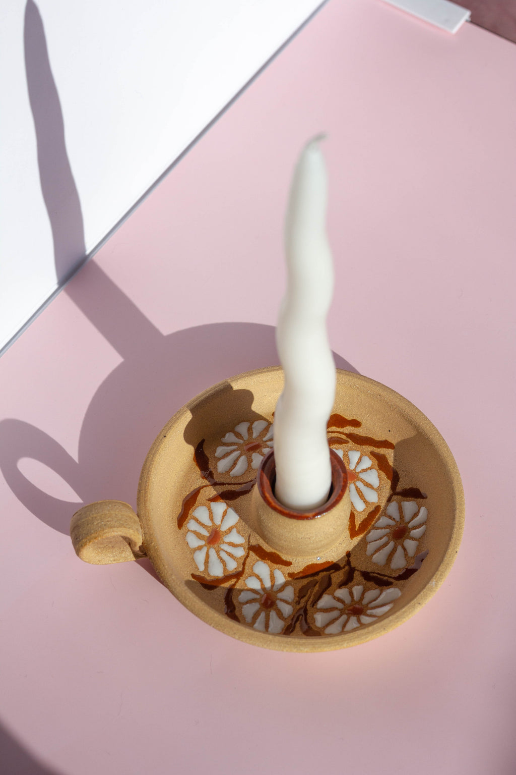 Decorative candle holder with a white candle on a pink surface